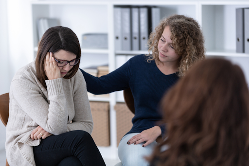 A woman helping an addict through recovery with a comforting hand on her shoulder. Wellbrook Recovery
