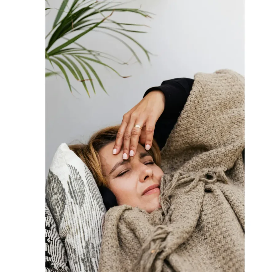 Woman suffering drug or alcohol withdrawal symptoms lying on a couch with eyes closed, wincing.