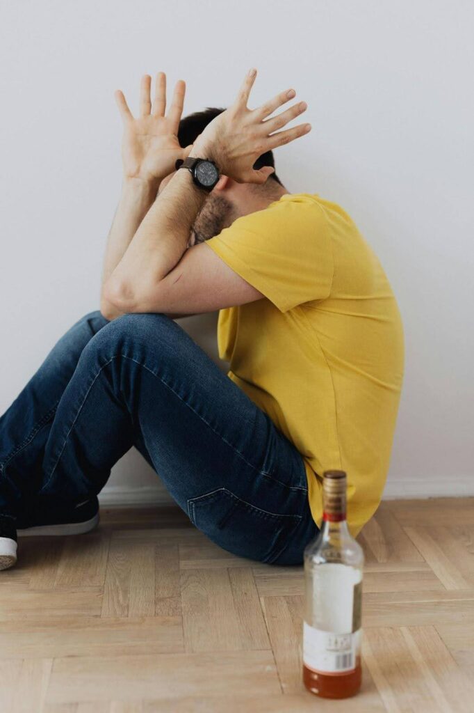 Man distressed on floor near a bottle, illustrating the challenges of detoxing from alcohol at home.