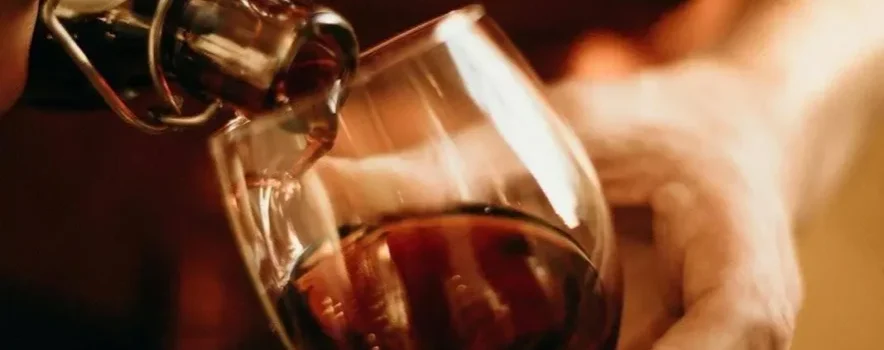 Person pouring wine into a glass, confronting the question “Can you detox from alcohol at home?”