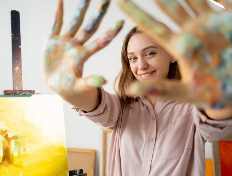 Person participating in art therapy, smiling with paint-covered hands in a creative addiction treatment setting.