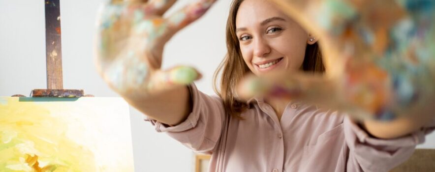 Person participating in art therapy, smiling with paint-covered hands in a creative addiction treatment setting.