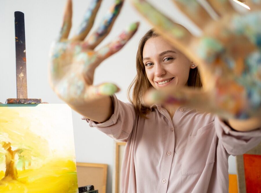 Person participating in art therapy, smiling with paint-covered hands in a creative addiction treatment setting.