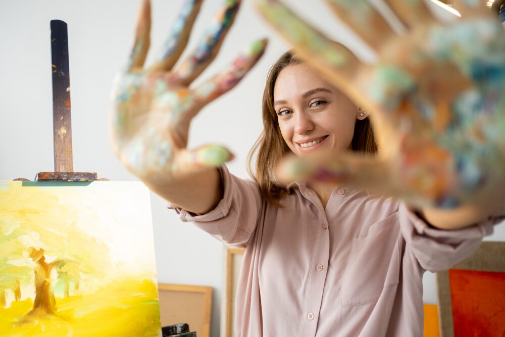 Person participating in art therapy, smiling with paint-covered hands in a creative addiction treatment setting.