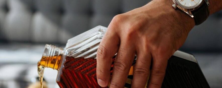 Man pouring whisky into a glass, illustrating signs of alcohol addiction