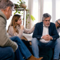 Senior friends offering support and empathy to a man experiencing sadness, sitting together in a comfortable home environment