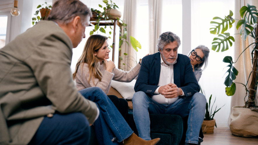 Senior friends offering support and empathy to a man experiencing sadness, sitting together in a comfortable home environment